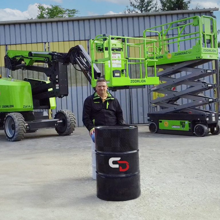 Commercial assis devant un chariot élévateur et une nacelle, près d'un baril noir.