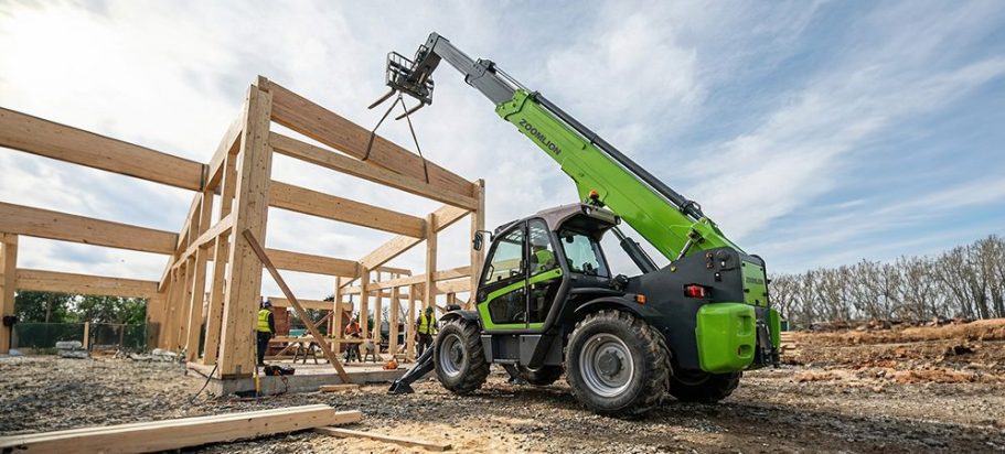 Chariot télescopique vert en train de soulever des poutres en bois pour un bâtiment.